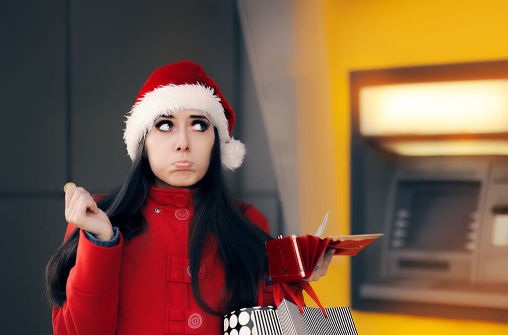 Dame mit rotem Mantel und Weihnachtsmannhut runzelt die Stirn, während sie die Brieftasche mit dem Geldautomaten im Hintergrund hält