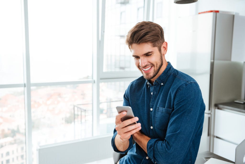 Foto de un joven usando un smartphone y sonriendo. Mirando el smartphone.